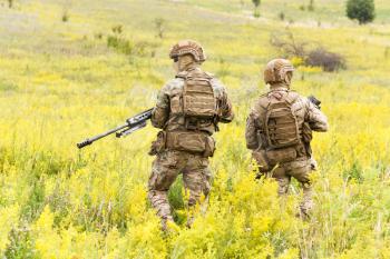 Two equipped and armed special forces soldiers with rifles in the blooming field