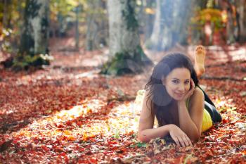 Pretty girl in the autumn forest laying on yellow leaves