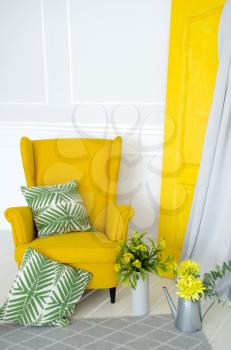 Yellow armchair in the interior with elements of home textiles, pillows and floral decor.