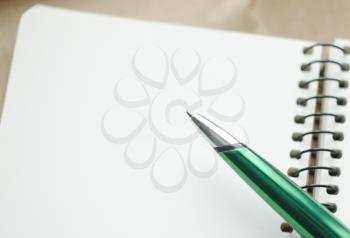 A part of open blank white notebook and green pen on the desk.