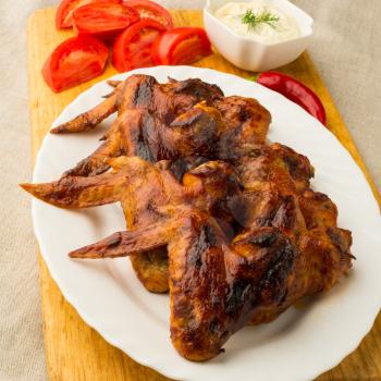 Crispy grilled chicken wings on white tarelkes vegetables and white sauce