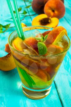 Iced green tea with peaches and mint in a glass on a turquoise wooden background, vertical, close up, selective focus