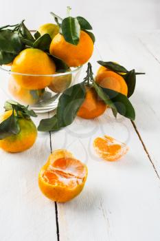 Ripe mandarines with leaves in a glass bowl on a white wooden background selective focus vertical