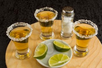 Gold tequila shots with lime and salt on the round wood board. Tequila. Gold Mexican tequila. Tequila shot. Alcohol  drink 