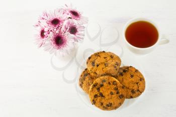 Romantic tea time with chocolate chip cookies. Homemade breakfast cookies and cup of tea served with lilac daisy