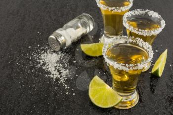 Shots of gold tequila with lime and salt on the black background. Tequila shot. Gold Mexican tequila. Tequila.