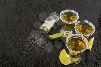 Tequila shots with lime and salt on black table. Tequila.  Gold Mexican tequila