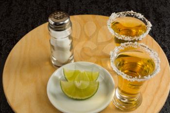Two gold tequila shots with lime and salt on the round wood board. Tequila. Gold Mexican tequila. Tequila shot. Alcohol  drink 