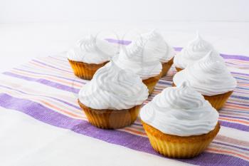 Row of white cupcakes on the striped  linen napkin. Homemade cupcakes with whipped cream.  Birthday cupcake. 