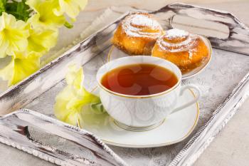 Sweet cinnamon bun rolls and cup of tea on vintage  serving tray. Breakfast Danish pastry and tea cup with yellow flowers. Breakfast tea with sweet pastry. 
