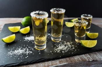Tequila shots with lime on black stone background. Strong alcohol  drink. Gold Mexican tequila shots. 
