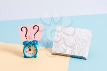 Mini size alarm clock beside a Paper sheet placed tilted on pastel backdrop