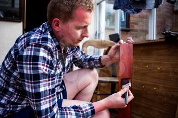Painting old wooden furniture. Housekeeper paints wooden boards with painting brush. Home improvements and renovations concept. Young man holds painting brush in his hands.