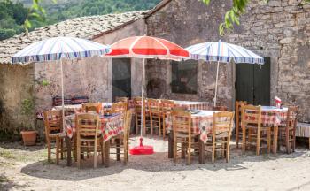 Colorful umbrellas covering the dining tables. Checkered pattern cloth lining the wood. Vacant lot offering food for customers. Country side restaurant set up