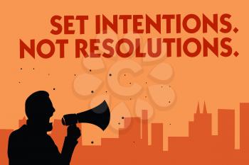 Text sign showing Set Intentions. Not Resolutions.. Conceptual photo Positive choices for new start achieve goals Man holding megaphone speaking politician making promises orange background