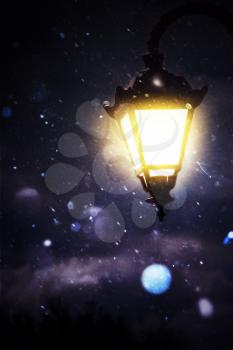 Lit up street lamp at snowy winter night close up, photo manipulation.