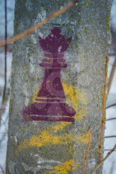 A chess piece of a queen is stamped on a cement pillar in the park.