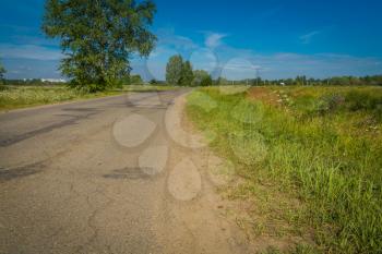 Old cracked, damaged asphalt road in countryside at sunny day.