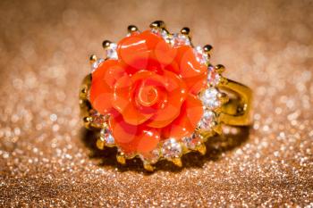 Fashion gold ring with natural orange coral in rose shape on glitter background.