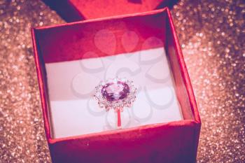 Silver amethyst ring in a red gift box on glittering background.
