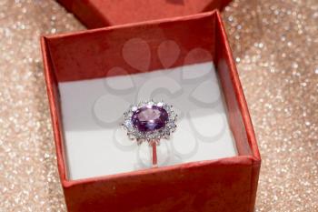 Silver amethyst ring in a red gift box on glittering background.