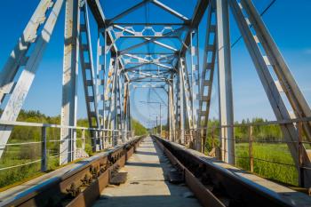 Metal railroad bridge in the countryside, clear blue sky background.