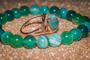 Modern gold ring and beaded bracelet made from green striped agate on glitter background.