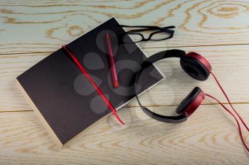 Headphones, notebook, pen and glasses on a wooden background