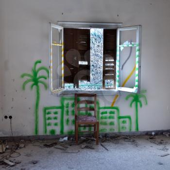 Chair and broken window in abandoned interior. City graffiti on the wall.