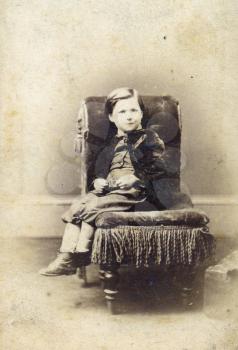 Portrait of Victorian young boy on chair. Sourced from antique cabinet card vintage photograph created by A.D. Lewis, Newcastle on Tyne, UK, circa 1870.
