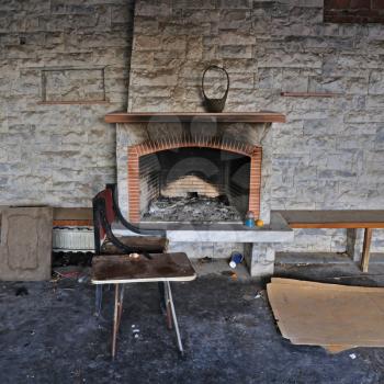 Chair and table close to dirty fireplace. Abandoned decayed house interior.