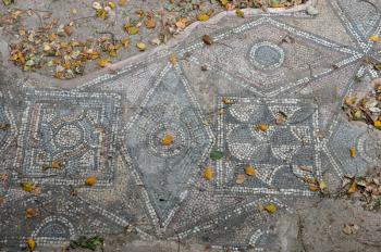 Ancient floor roman mosaic geometric shapes motif abstract pattern and fallen leaves. Athens, Greece.