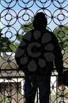 Hooded man looking at view from the balcony of an abandoned house and vintage iron gate circles pattern.