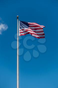 A photo of the American flag on a long pole with blue sky behind.