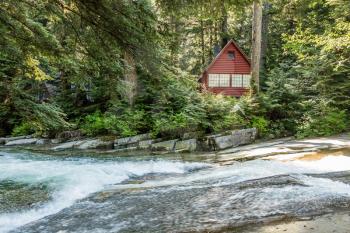 Clear water rushes along  on Denny Creek in Washington State. An A-frame cabin is in the background.