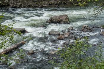 The Snoqualmie River flows past a rock creating white water.