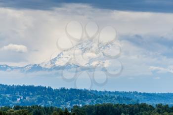 Mount Rainier is surrounded by clouds with trees below.
