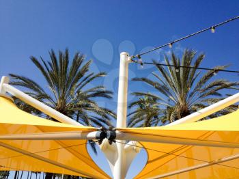 Yellow mesh canvas shade canopies and palm trees on sunny day