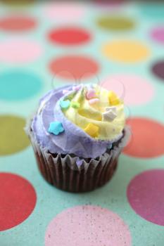 Easter yellow and lilac chocolate cupcake with candies on a colorful giant polka dots background