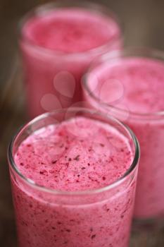 Three strawberry smoothies in a row on a wooden background