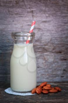 Almond milk in a  bottle with strip straw and fresh almond on a wooden surface