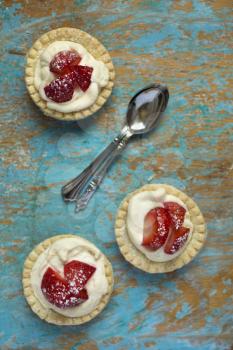 Top view of strawberry tartlets with spoons on a grunge background
