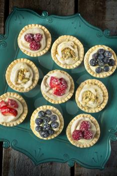 Strawberry, blueberry and pistachios tartlets on green tray on a wooden table