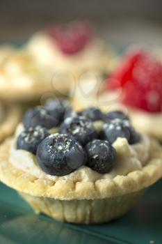 Blueberry, strawberry and pistachios tartlets on green tray on a wooden table