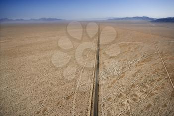 Aerial view of two lane highway in desert with mountains in background.