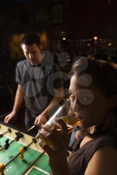Royalty Free Photo of a Young Woman Drinking Beer While a Man Plays Foosball in a Pub