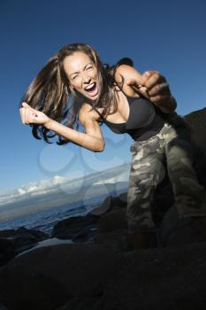 Royalty Free Photo of a Woman at a Rocky Beach Leaning into a Camera Holding Out Fists and Yelling