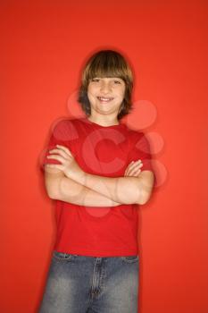 Royalty Free Photo of a Portrait of a Boy in Studio Standing Against a Red Background With Arms Crossed