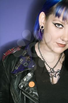 Portrait of Caucasian woman with blue hair and black leather jacket against blue background.