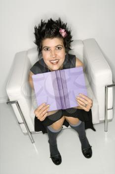 Royalty Free Photo of a Woman Sitting in a Chair Holding an Open Book